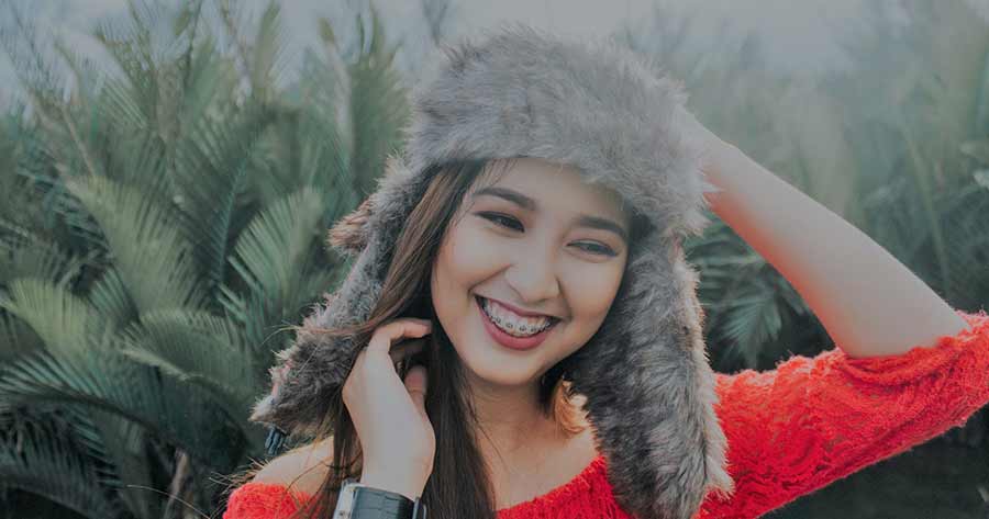 A photo of a smiling woman in a red shirt wearing a gray fur beanie